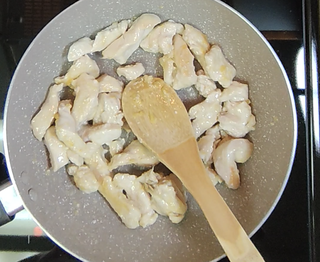 Chicken breast strips cooking in a frying pan with a wooden spoon