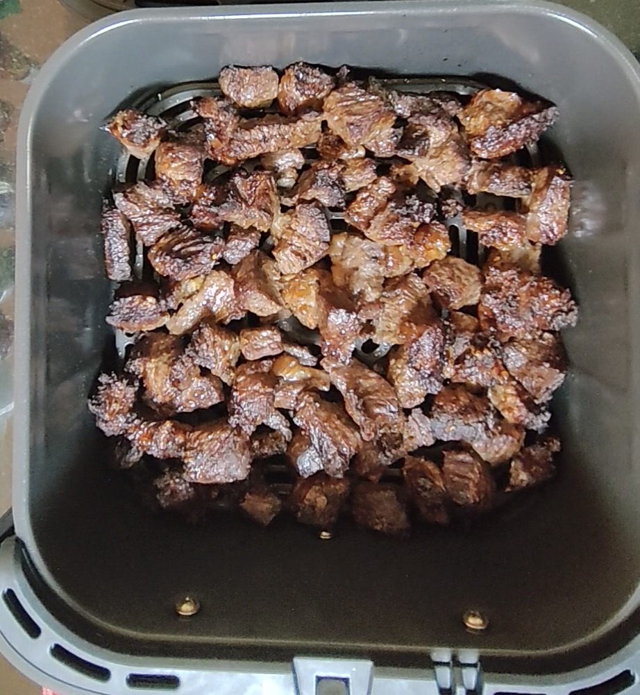 Browned beef cubes on the crisper plate in an air fryer basket partway through cooking
