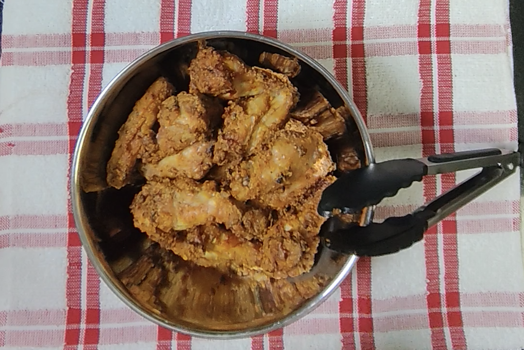 Cooked chicken wings transferred to a metal mixing bowl with tongs