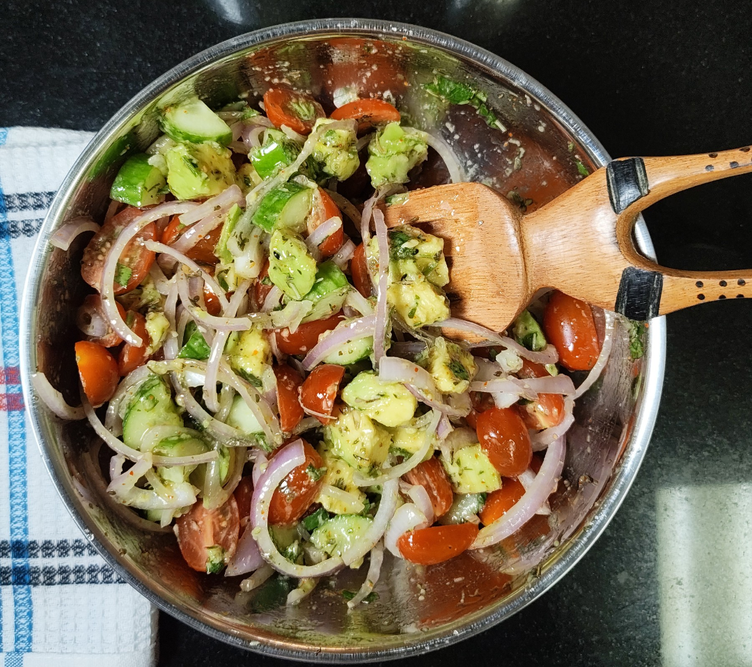 Esther Lackie's tossed avocado, tomato and cucumber salad with sliced onion and herb dressing in a metal bowl with a wooden serving fork