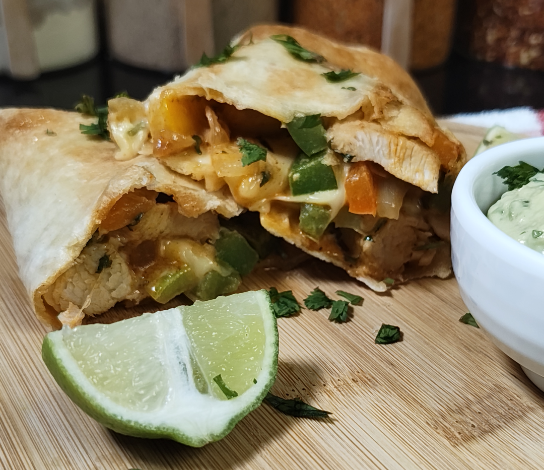 Close-up of a halved chicken fajita wrap with melted cheese, peppers and chicken, a lime wedge and homemade guacamole