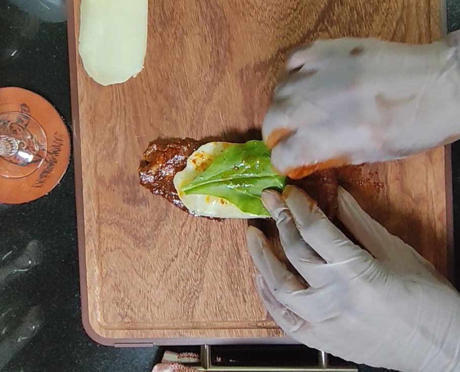 Mozzarella cheese and fresh baby spinach placed onto seasoned beef on a wooden board before rolling