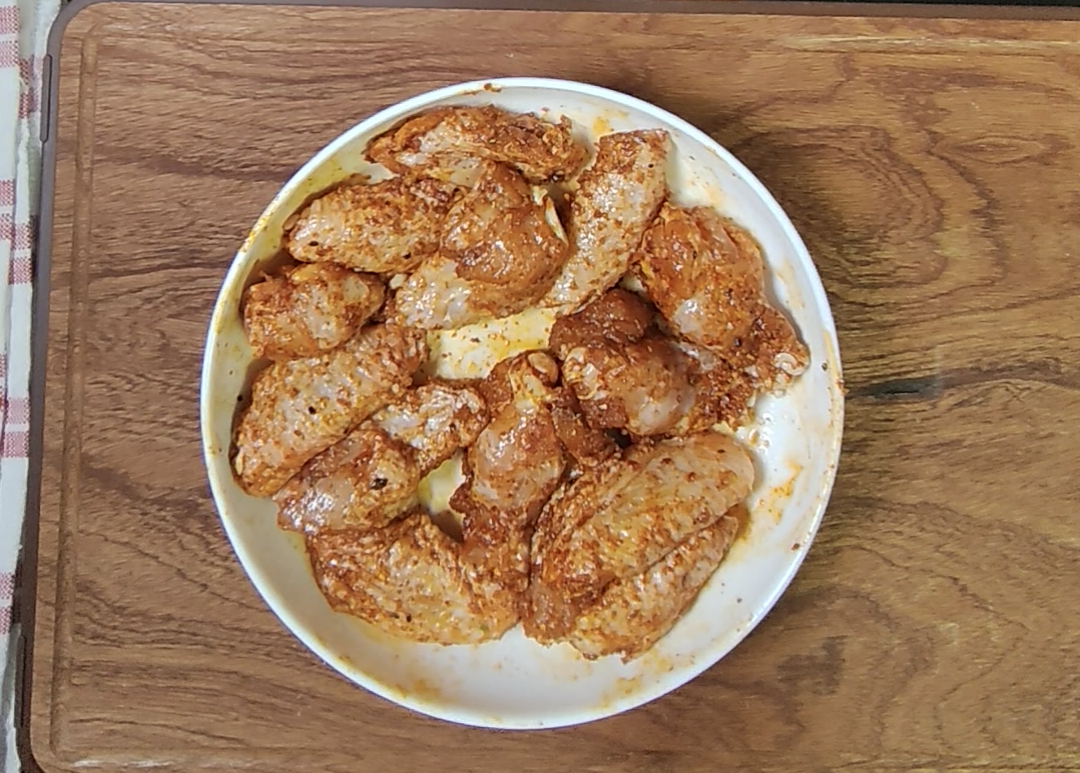 Raw chicken wings coated in the red dry seasonings in a mixing bowl